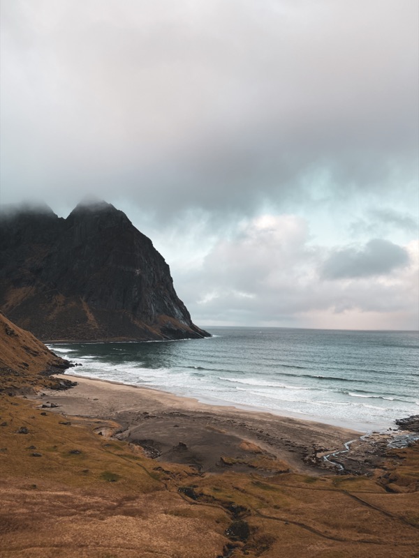 Dramatic beach scene in Lofoten with a sharp mountain peak and moody clouds